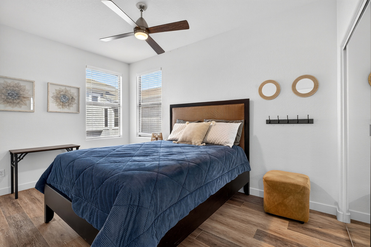 Queen bedroom with ceiling fan, closet storage, side table, and natural light from the corner windows.