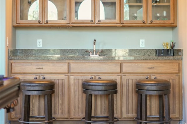 Built-in wet bar with granite countertop, glass-front cabinets, and bar seating—ideal for post-game drinks.