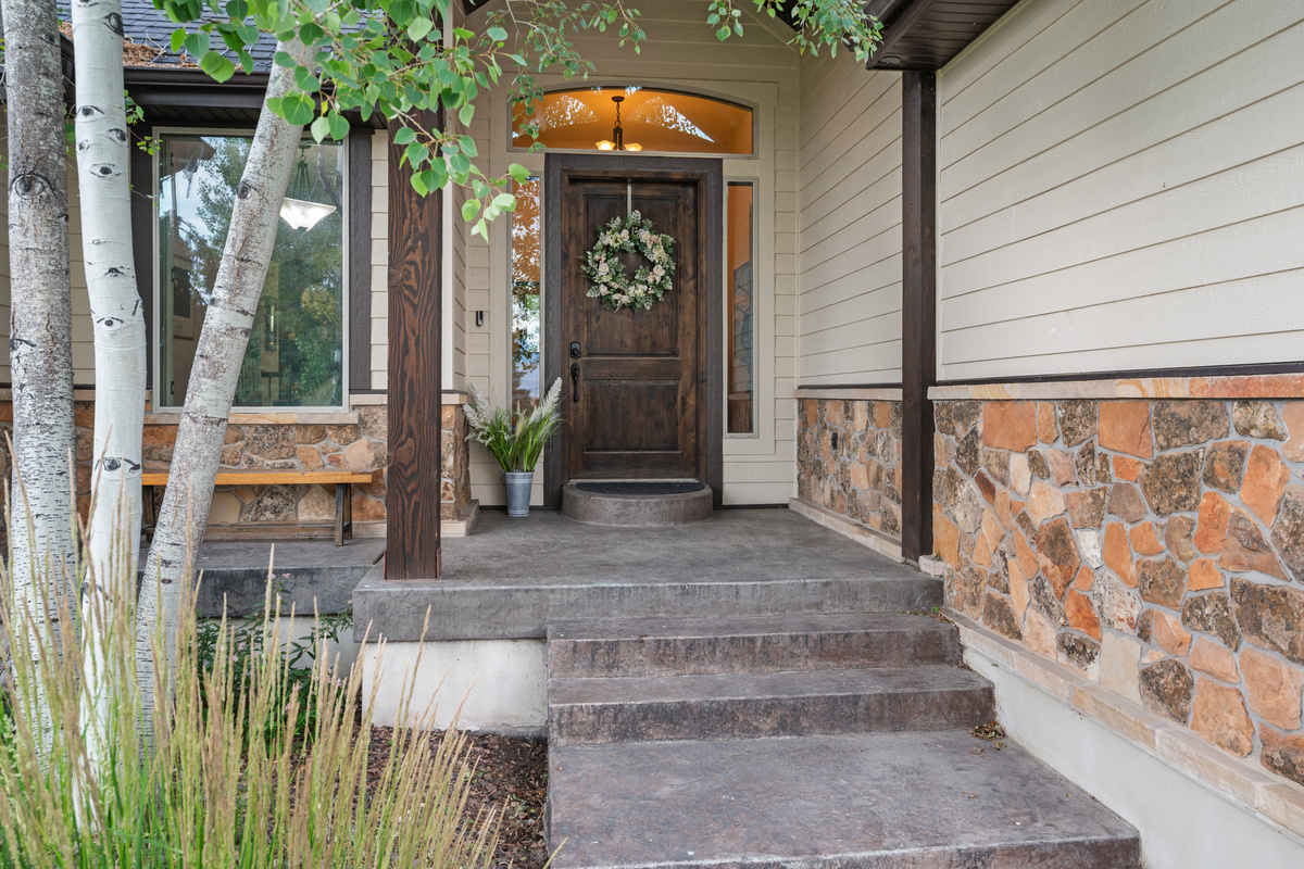 A warm mountain welcome begins at the inviting front porch, surrounded by mature landscaping and rustic stone accents.