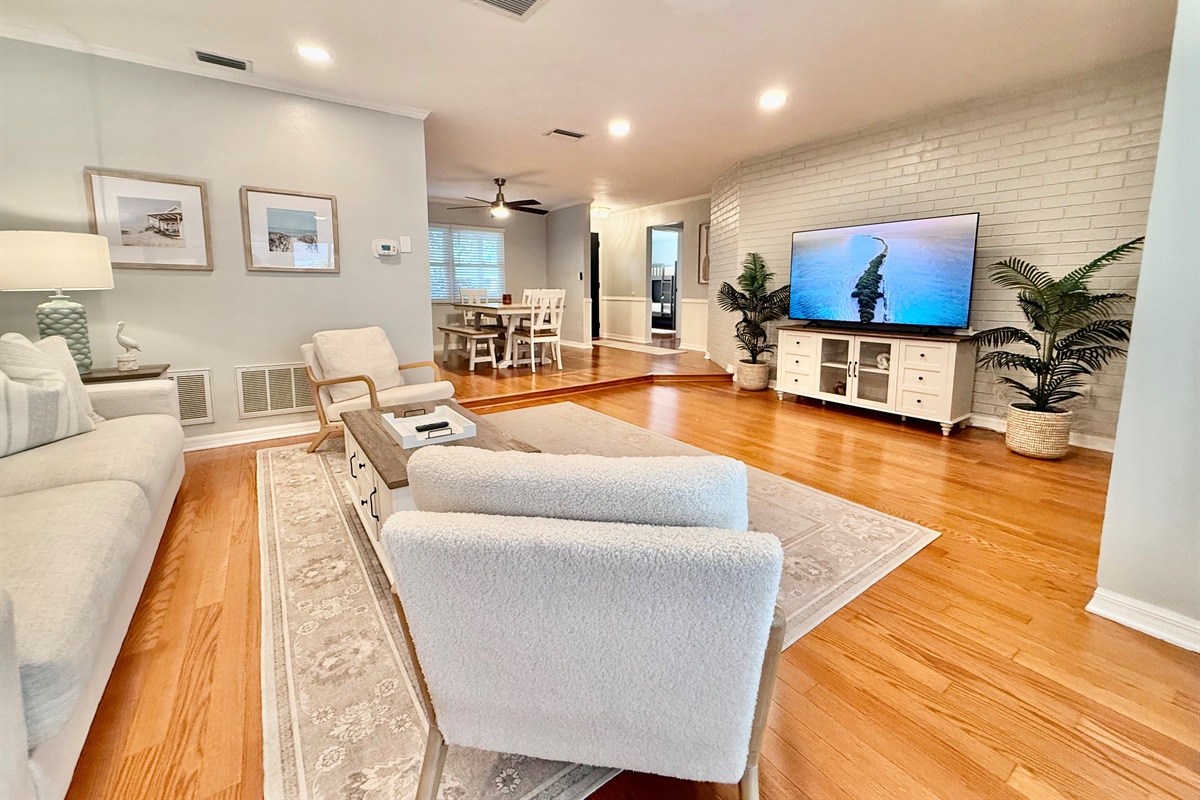 Stretch out and unwind in this spacious living area featuring warm wood floors, serene tones, and comfy furniture perfect for family time or movie night.