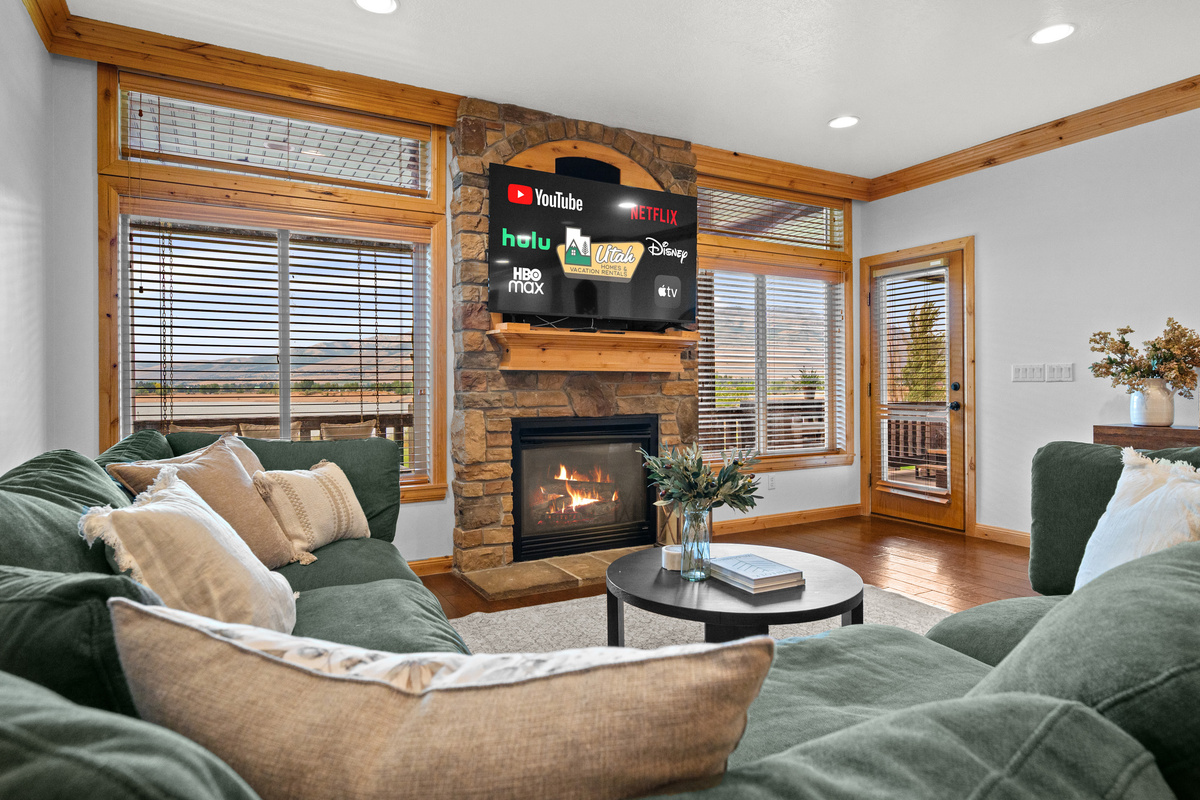 Cozy living room featuring lake views, a stone fireplace, large windows, and warm natural light.