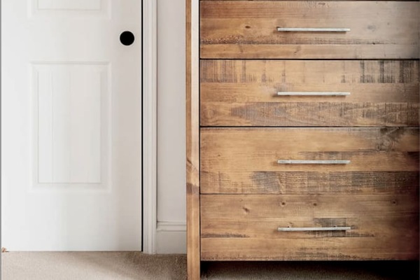 This close-up features a tall dresser made of rustic wood with horizontal silver-tone handles. It sits next to a generous sized closet.