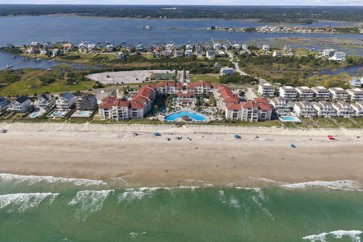 Aerial overview of the beachfront resort layout, highlighting the pool courtyard, sandy shoreline, and soundfront backdrop.