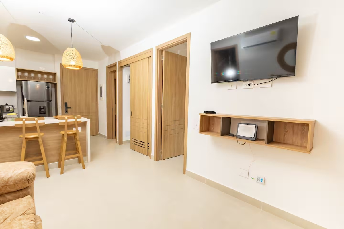 Sala de estar compacta con TV montada en la pared, asientos en la barra de desayuno y la cocina cercana para una estancia sencilla y práctica en el apartamento.