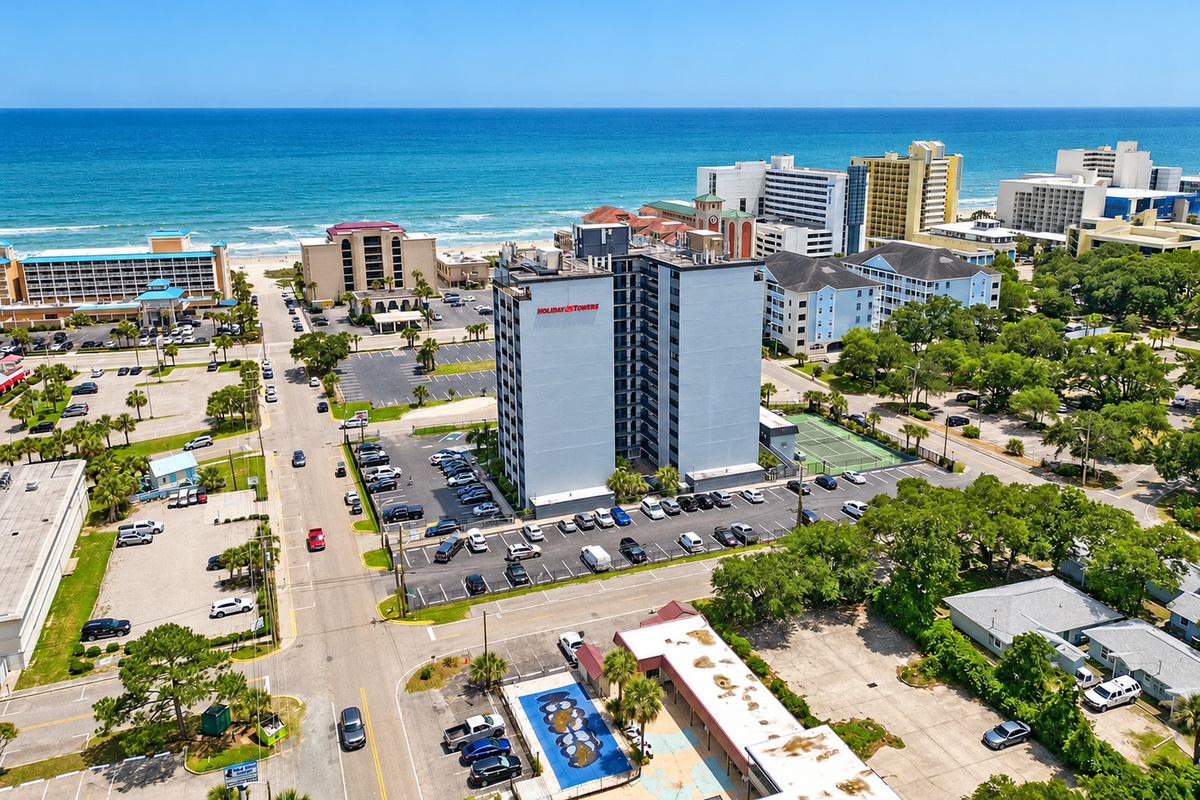Aerial view of Holiday Towers with shared pool, hot tub, sports court, parking, and Myrtle Beach attractions nearby.