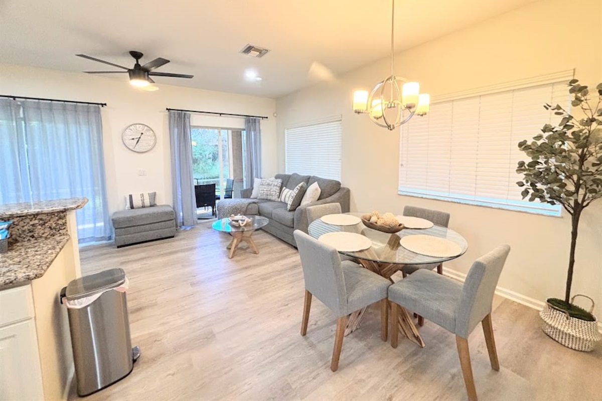 Bright and stylish dining and living area with modern furnishings, wood-look flooring, comfortable seating, and sliding glass doors leading to the outdoor space.