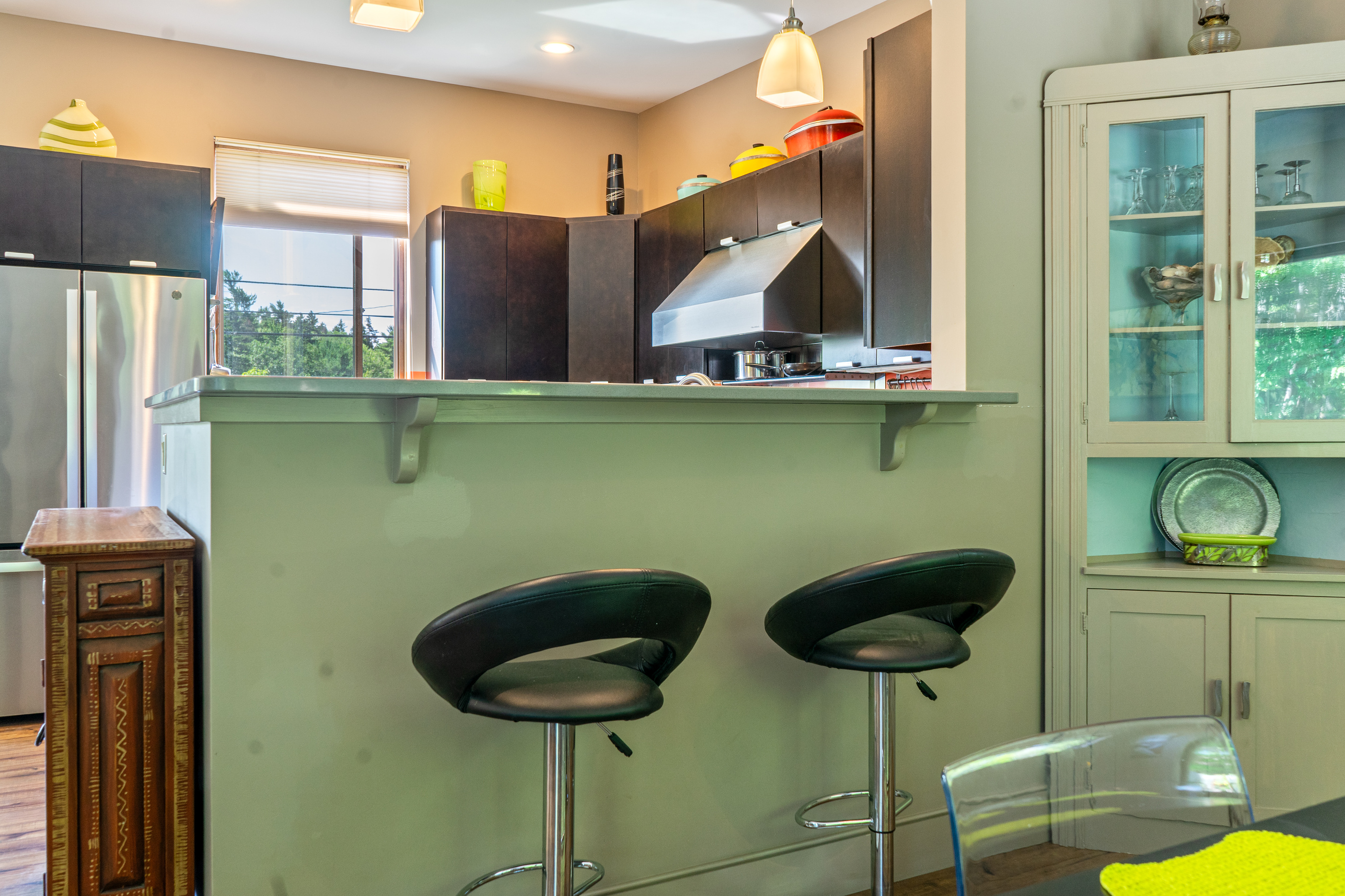 Social connectivity in the main living space. A raised breakfast bar with sleek swivel stools anchors the kitchen-to-dining transition at "The Crag," featuring built-in hutch display storage and an open, conversational layout.