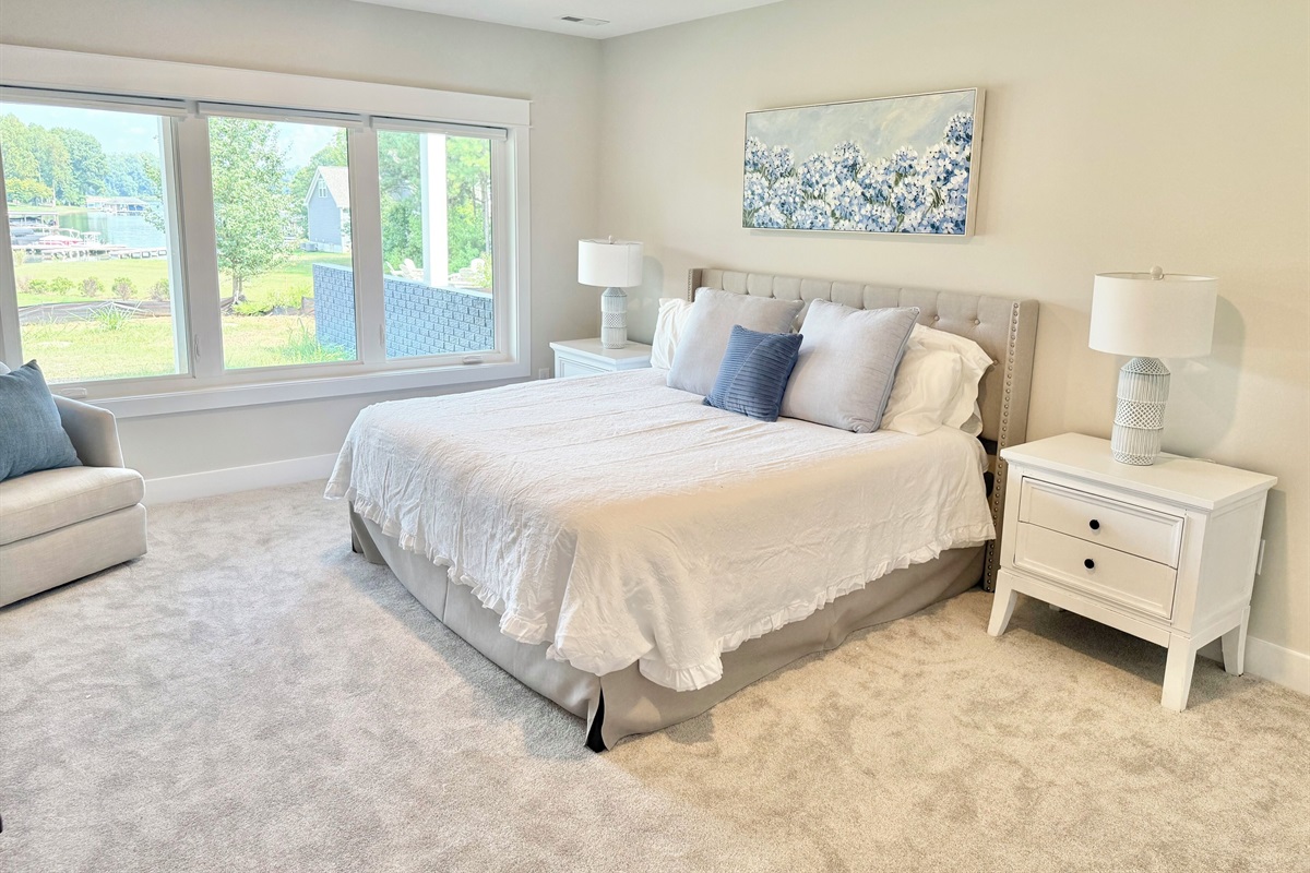 The king "Hydrangea Room" is  finished in soft grays, whites, & blues, featuring luxury bedding, a plush white comforter, and a feathery soft bed. Expansive windows offer stunning lake views. Every detail is curated to offer guest that retreat feel!