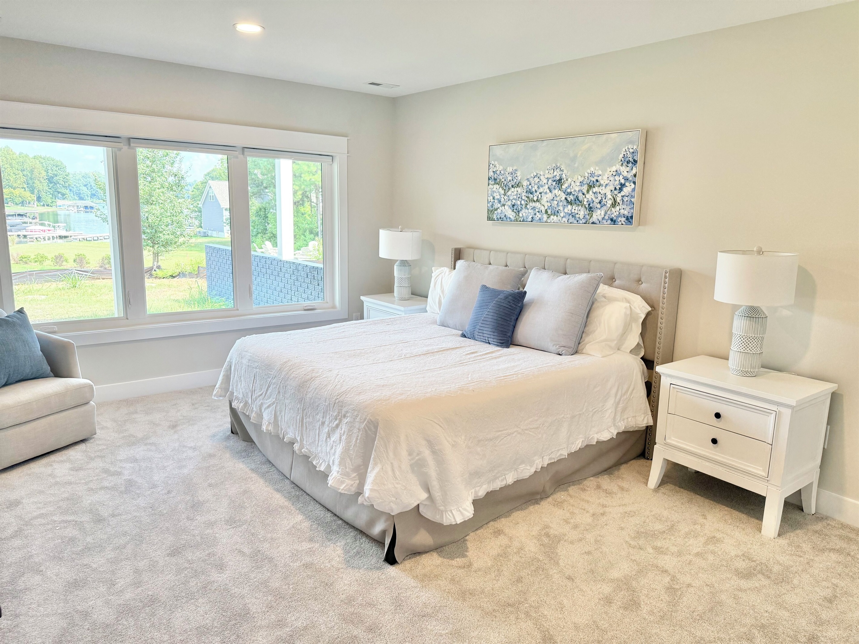 The king "Hydrangea Room" is  finished in soft grays, whites, & blues, featuring luxury bedding, a plush white comforter, and a feathery soft bed. Expansive windows offer stunning lake views. Every detail is curated to offer guest that retreat feel!