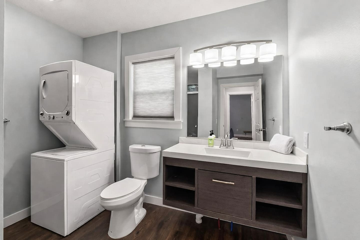 Modern full bathroom featuring a sleek vanity, bright lighting, toilet, and in-unit washer and dryer for added convenience.