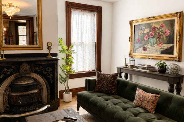 The main living room — an original cast iron fireplace with gold inlay, green velvet sofa, and a gilded mirror that catches the original stained glass window perfectly. Some combinations just work.