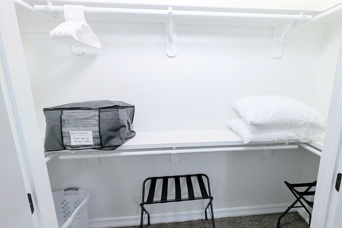 Primary closet is stocked with hangers, extra pillows and blankets, luggage racks, and a laundry hamper.