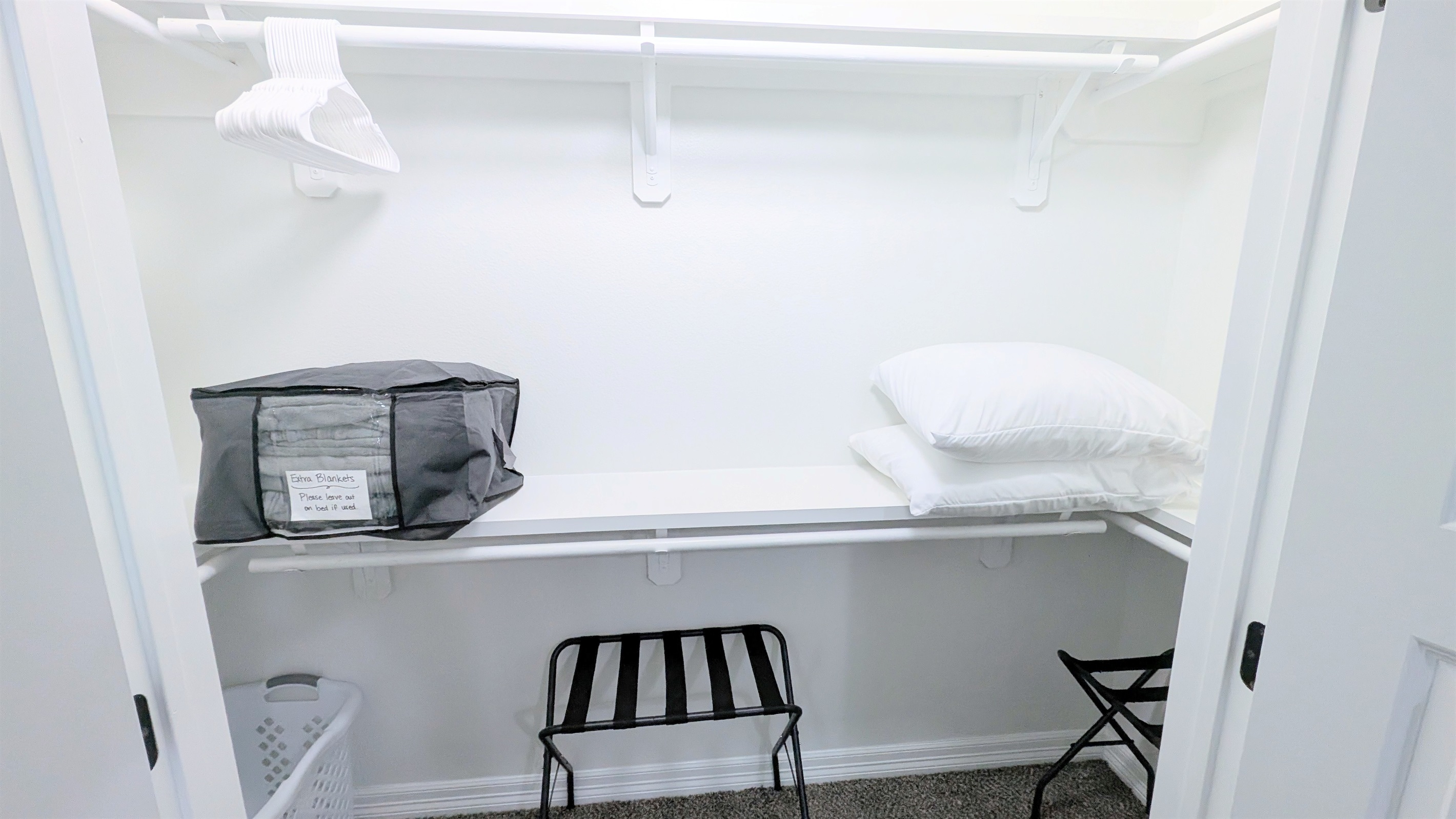Primary closet is stocked with hangers, extra pillows and blankets, luggage racks, and a laundry hamper.