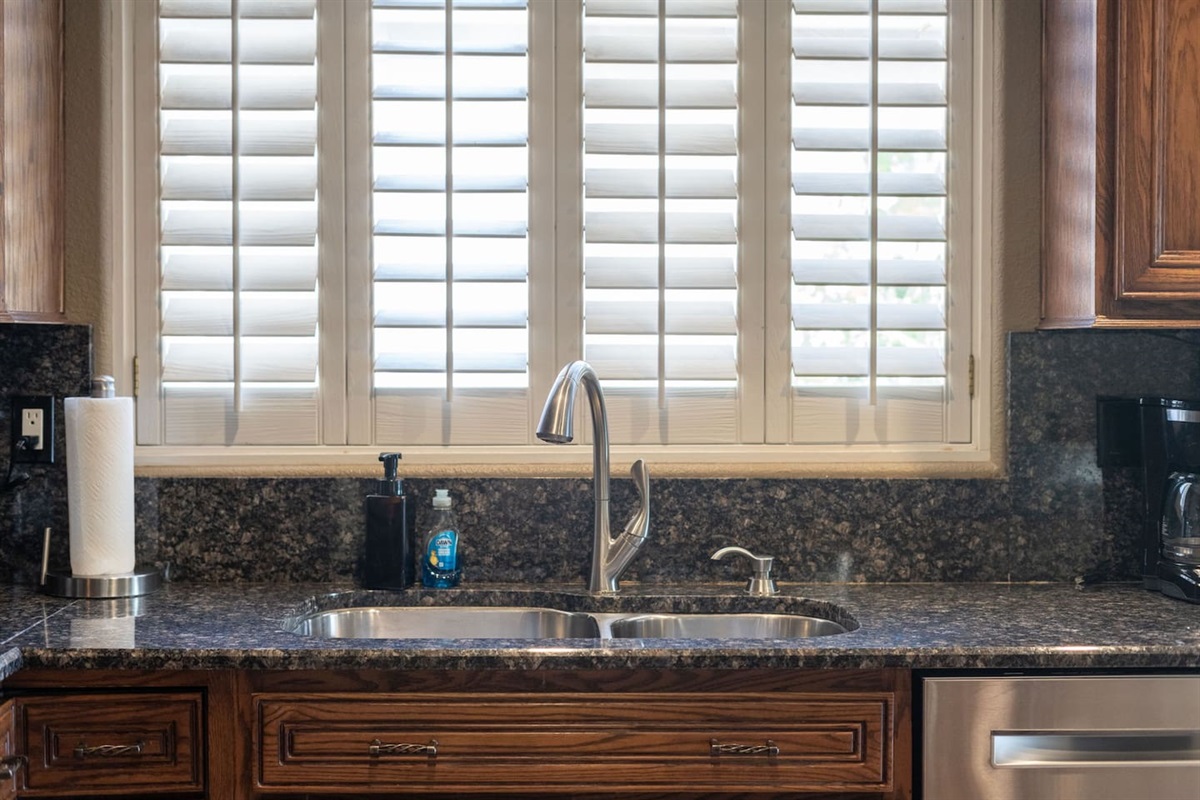 A bright, clean sink framed by plantation shutters lets in just the right amount of light — a pleasant spot to prep and clean up.