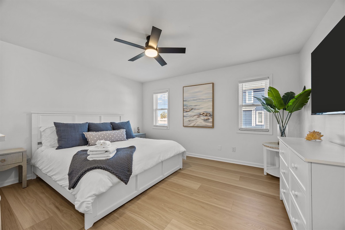 Spacious first-floor master bedroom featuring a king bed, TV, and bright windows: perfect for guests who prefer main-level living