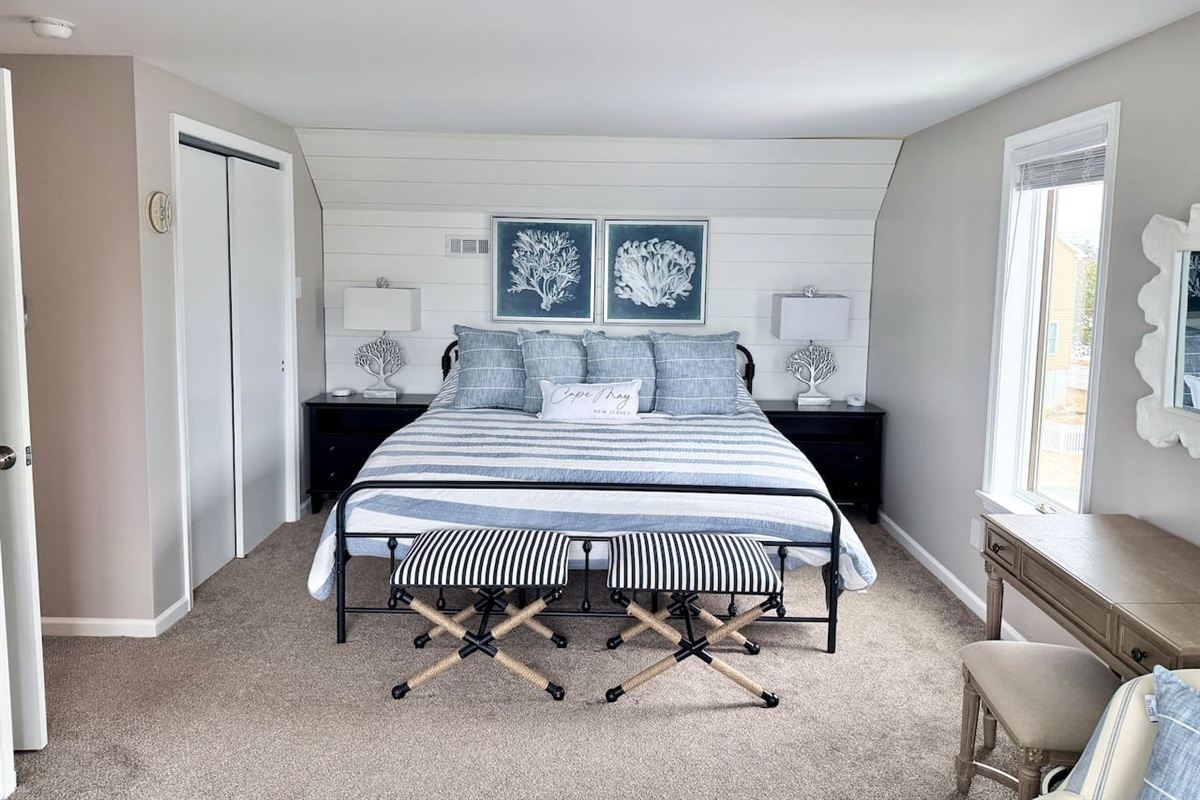You will find a serene bedroom retreat designed with a calm, coastal aesthetic. The space features a cozy bed adorned with blue and white accents, framed by a charming shiplap wall, making it an ideal, restful sanctuary for your vacation.