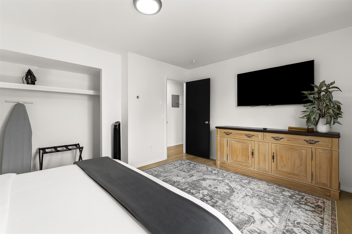 Wide view of the primary bedroom featuring a Smart TV, dresser, and blackout curtains for comfort and privacy.
