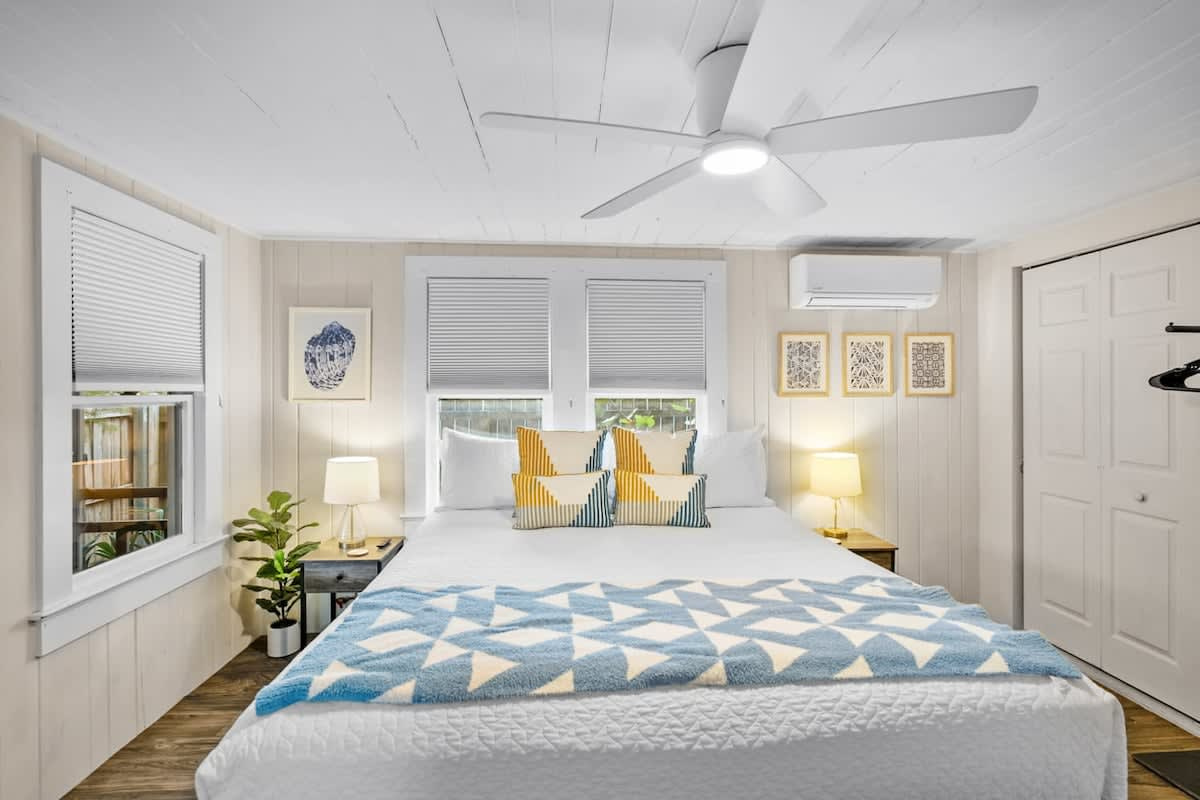 The bedroom is calm where the rest of the cottage is loud, with a king bed beneath a slowly turning ceiling fan. Shutters and blinds close the morning out for as long as the holiday will let you sleep.