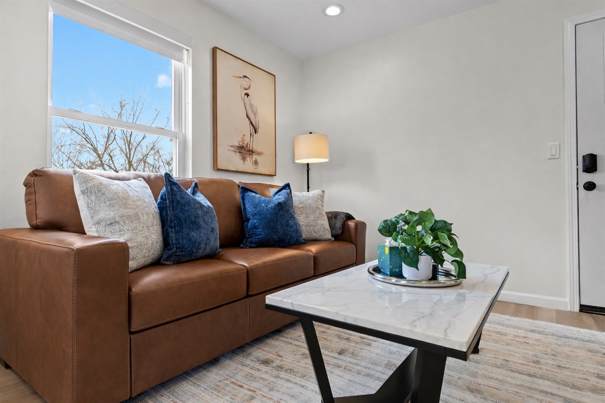 Sun-filled living room with a plush leather sofa, stylish décor, and calming artwork—an inviting spot to relax, recharge, and enjoy the natural light.