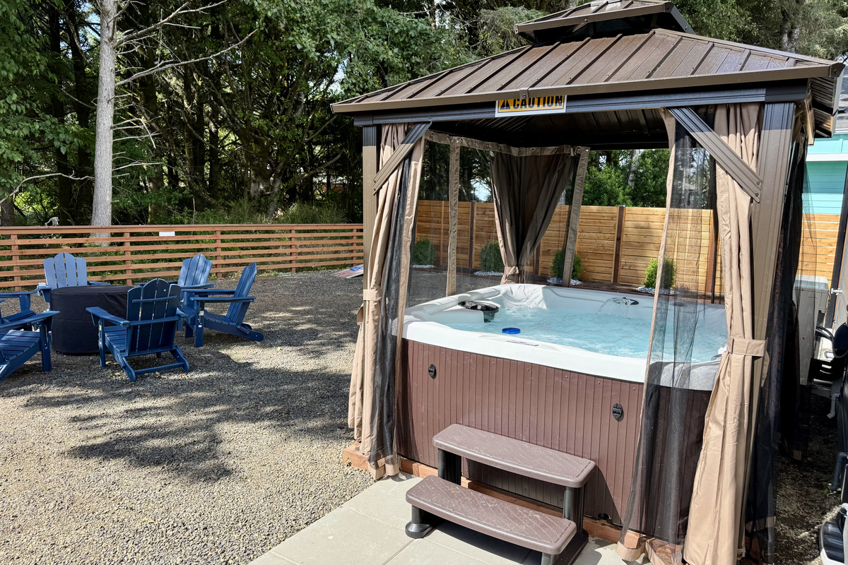 Two private 6-person hot tubs, one per side. The Speakeasy side's sits under a curtained gazebo with the fire pit chairs right beside it.