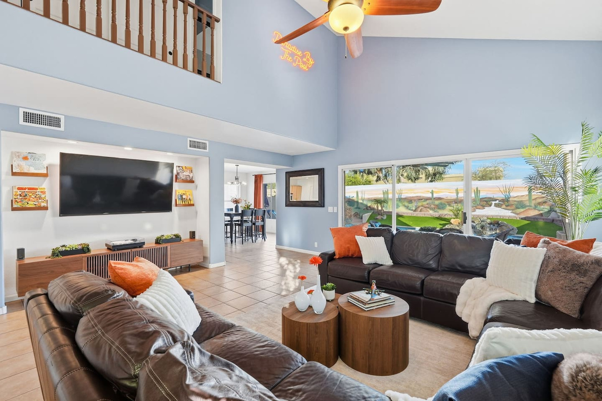 Living room with vaulted ceilings, large TV, sectional seating, and wide windows overlooking the pool 