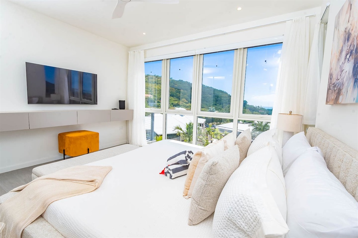 Master bedroom with king size bed, en-suite bathroom, air conditioning, ceiling fan, wall mounted tv, closet and gorgeous views of the ocean and hillside.