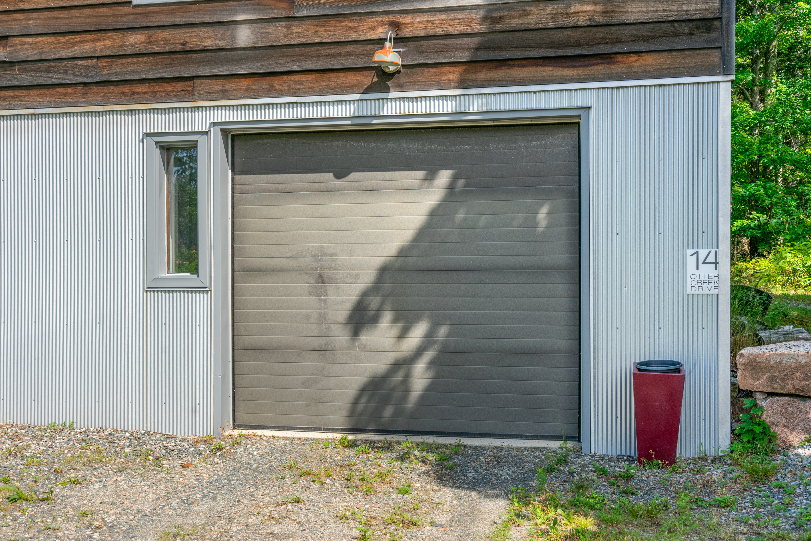 Industrial corrugated metal frames "The Crag's" ground-level garage entrance. Designed for functional storage and sleek modern aesthetics, anchoring the base of this vertical retreat right on the Acadia border.