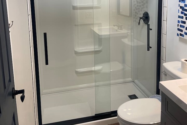 This updated bathroom features a spacious walk-in shower with sleek glass doors and matte black fixtures. Clean white tile, warm wood flooring, and modern lighting create a fresh, spa-like feel—perfect for relaxing during your short-term stay.