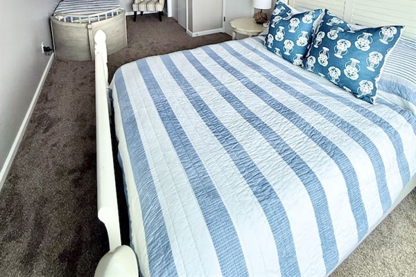 This family-friendly bedroom features a white bed dressed in a blue and white striped quilt, accented by decorative patterned pillows. The space also includes a charming, curved boat-style bed perfect for children.