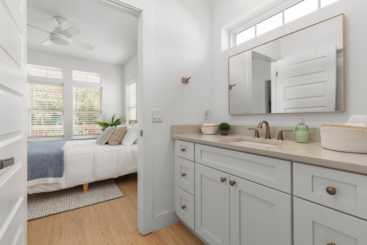The bathroom opens straight off the bedroom, so the trip from bed to shower runs about four steps. A long counter, a wide mirror, and high windows letting the morning light in over the top of all of it.