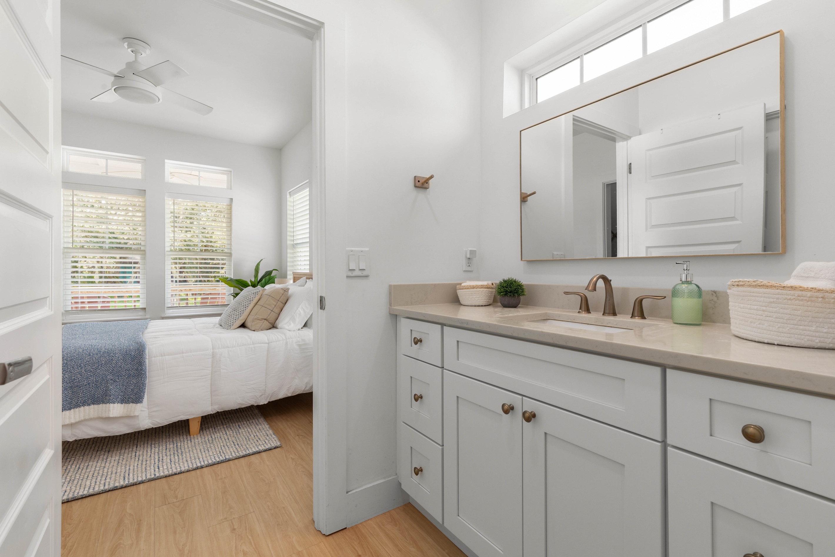 The bathroom opens straight off the bedroom, so the trip from bed to shower runs about four steps. A long counter, a wide mirror, and high windows letting the morning light in over the top of all of it.