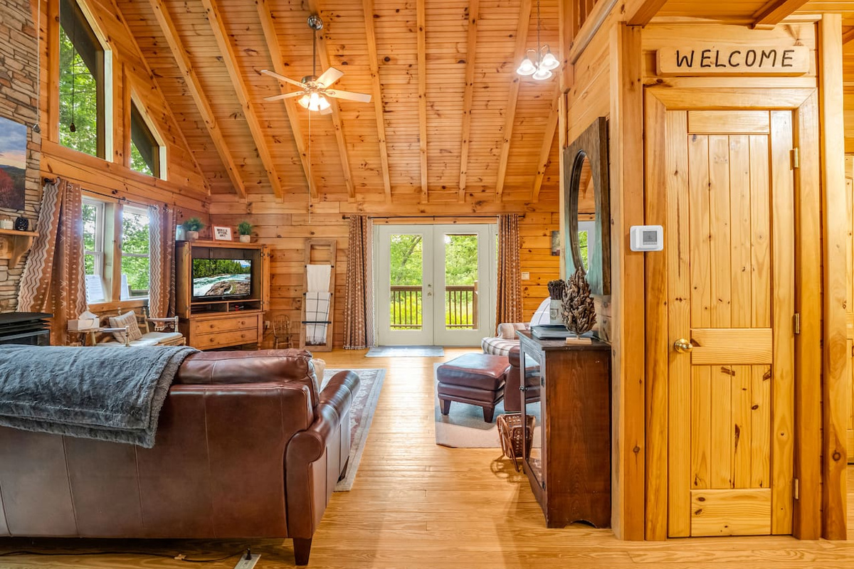 Spacious main living room area with soaring wood ceilings, comfortable seating, and deck access with overlooking trees