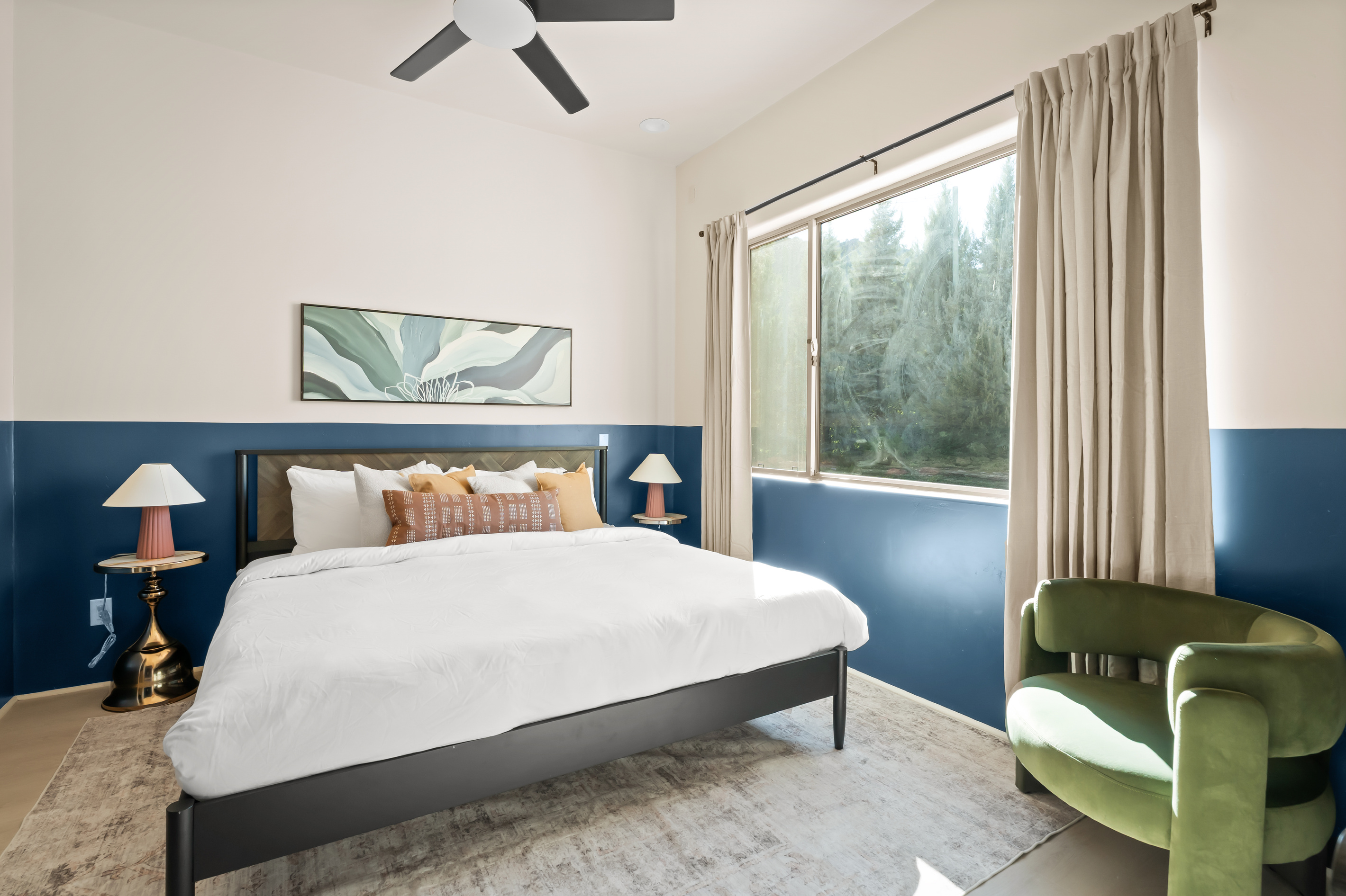 Spacious suite framed by oversized picture windows looking out onto the greens—complete with a velvet accent chair and ceiling fan.