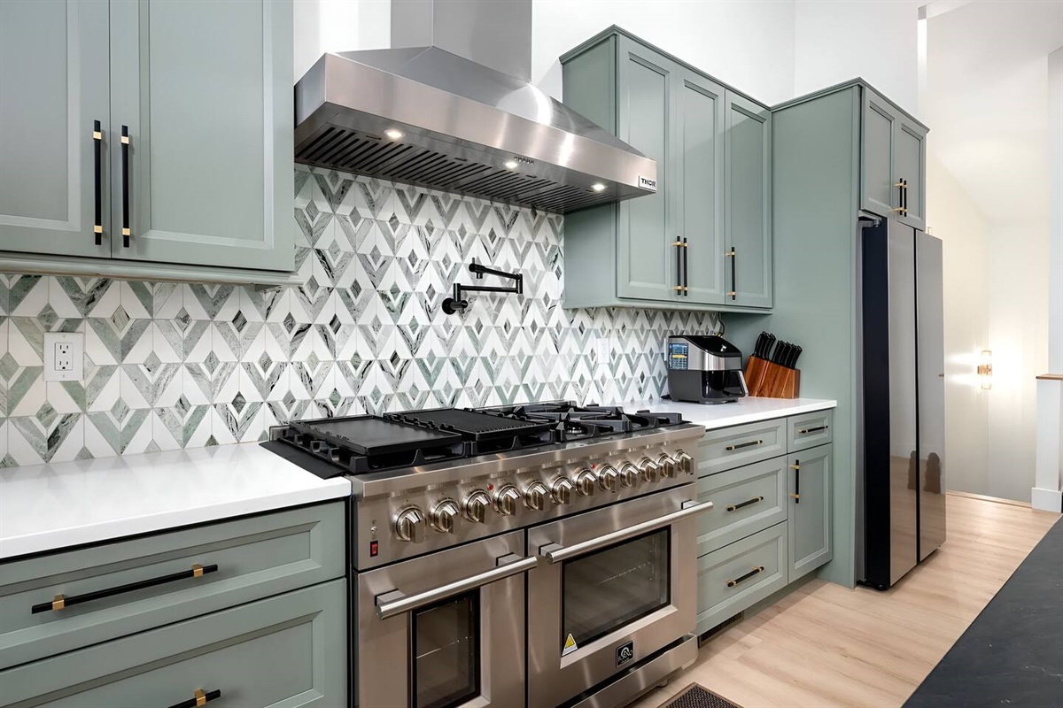 A spacious, chef-inspired kitchen featuring stainless steel gas range, custom sage cabinetry, quartz countertops, and a designer tile backsplash. Perfect for cooking, entertaining, and extended stays.