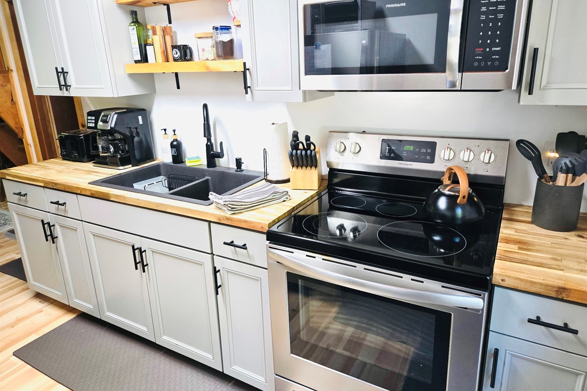 Galley kitchen with stove, microwave, refrigerator, toaster, dual coffee maker.