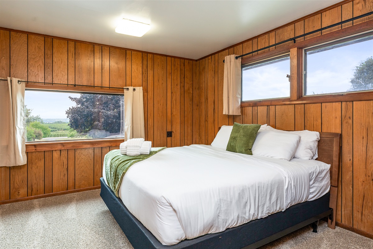 Cozy bedroom with warm wood accents, plush bedding, and a large window framing scenic views—an inviting retreat.
