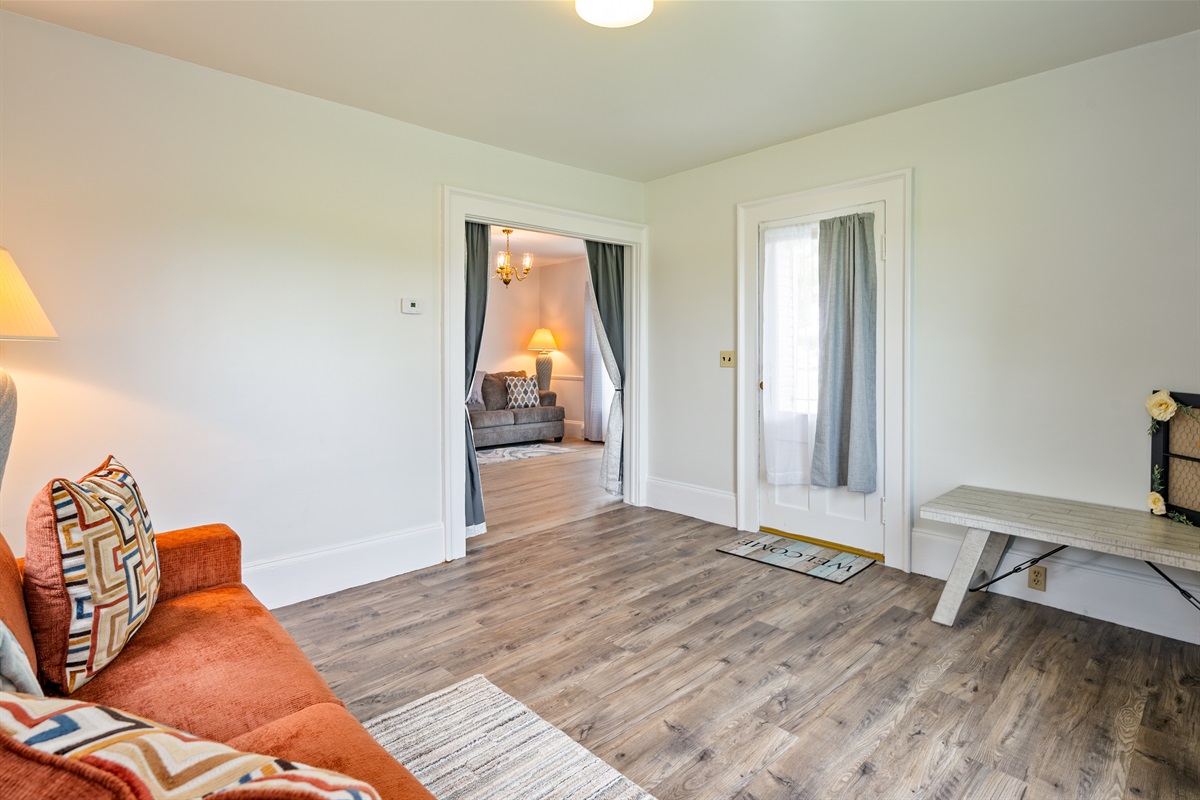 This bonus lounge offers a cozy spot to unwind, featuring an orange sofa, rustic bench, and direct access to the main living room.