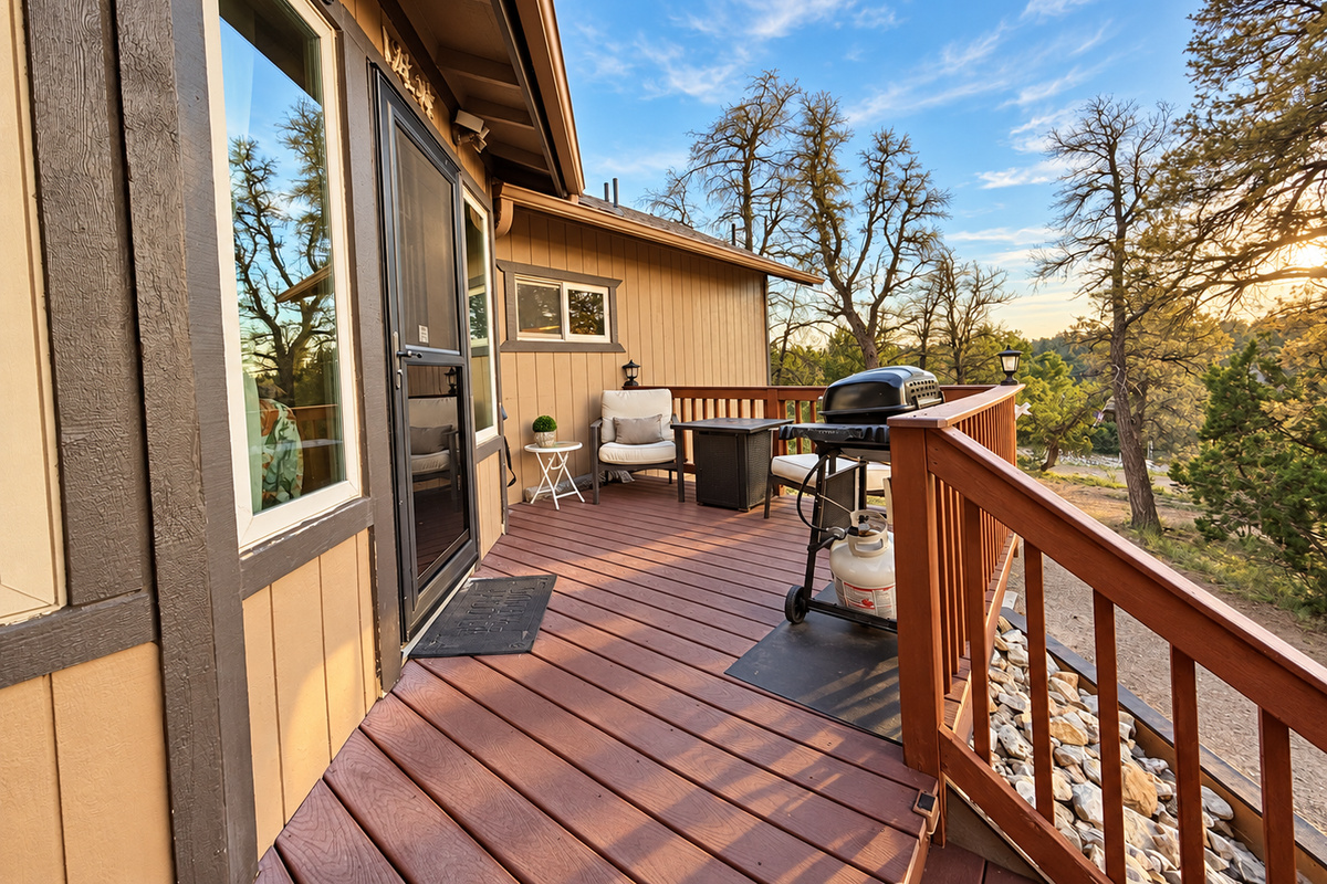 Deck surrounding entry features cushioned chairs, propane grill and umbrella. The perfect spot for enjoying white mountain skies and views.