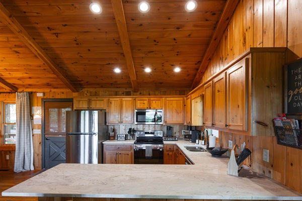 Fully stocked kitchen with stainless steel appliances, quartz countertops, and island seating - perfect for cooking, gathering, and staying in.