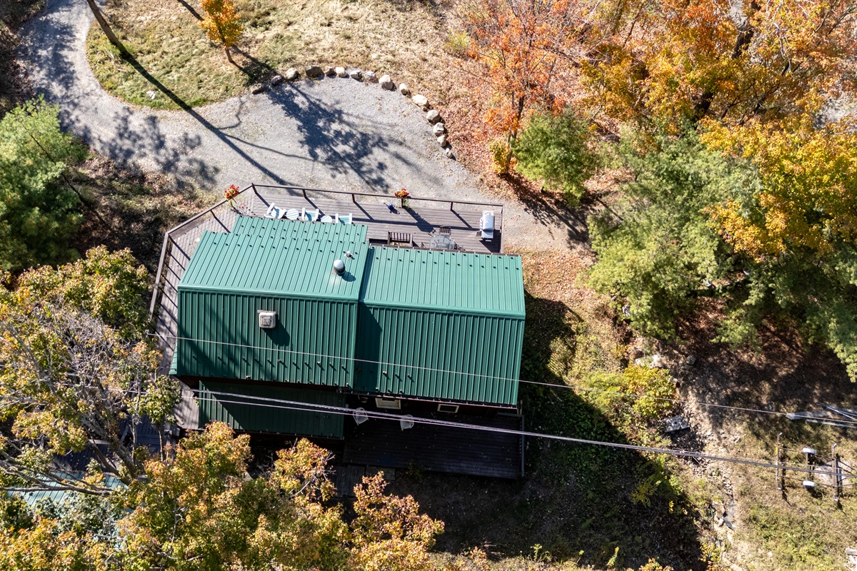 Aerial shot showing the green metal roof and wooded driveway of the cabin.