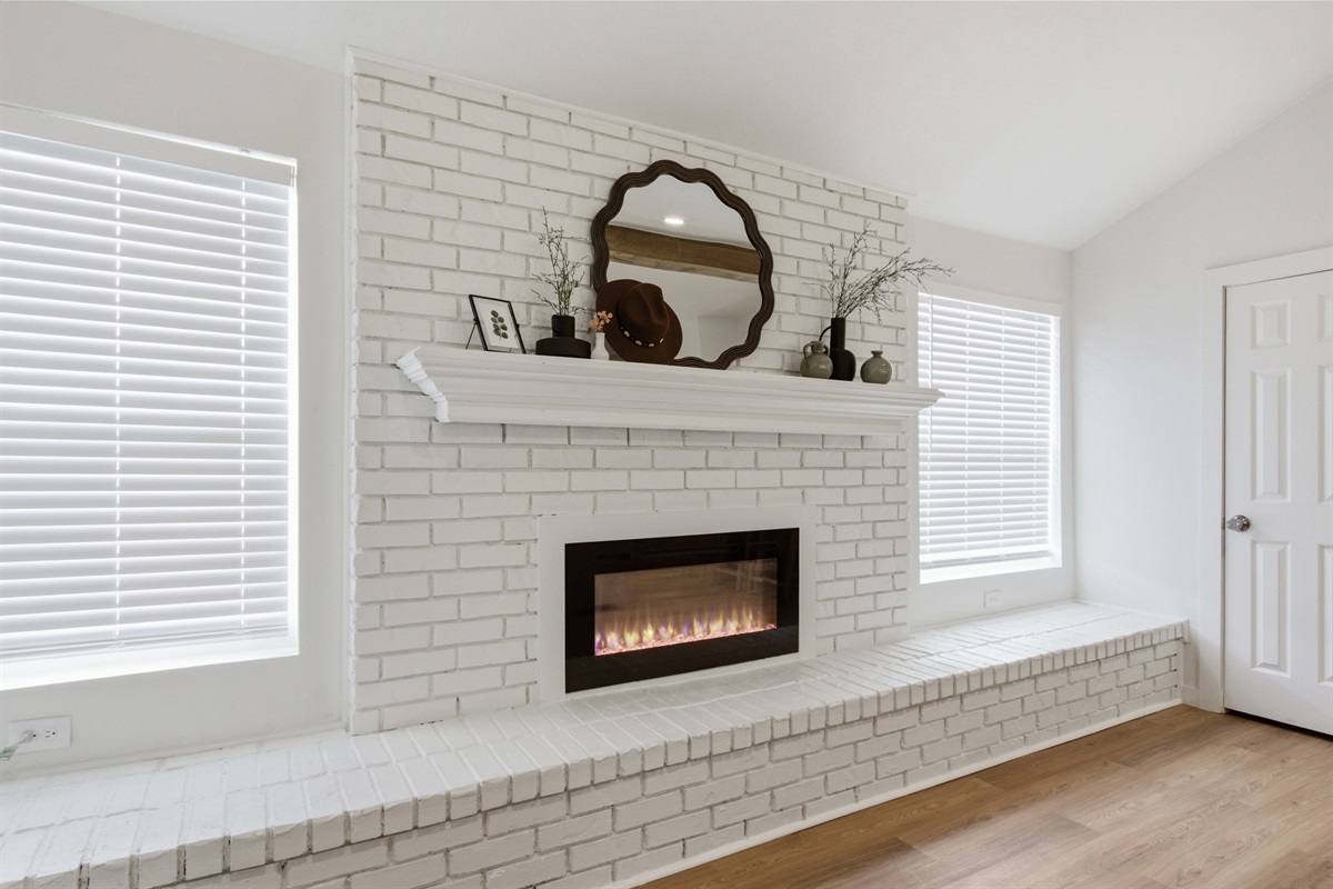 Decorative fireplace with brick surround and round mirror. Living room focal point in this 4-bedroom Arlington vacation rental.