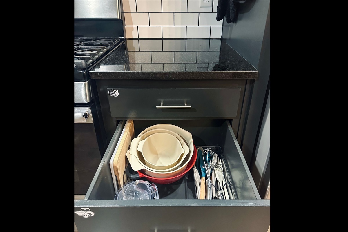 Kitchen drawer thoughtfully stocked with cutting boards, mixing bowls, liquid measuring cups, and essential cooking utensils for effortless meal prep.