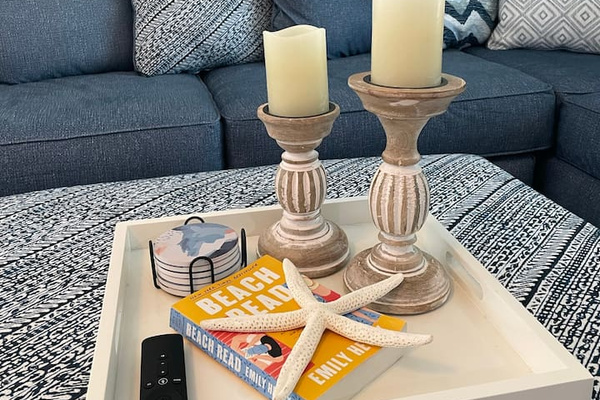 Beach Read on the tray, remote within reach — evenings here shuffle between candlelit conversation and one more episode, with the big ottoman doubling as a footrest for however many feet show up to claim it.