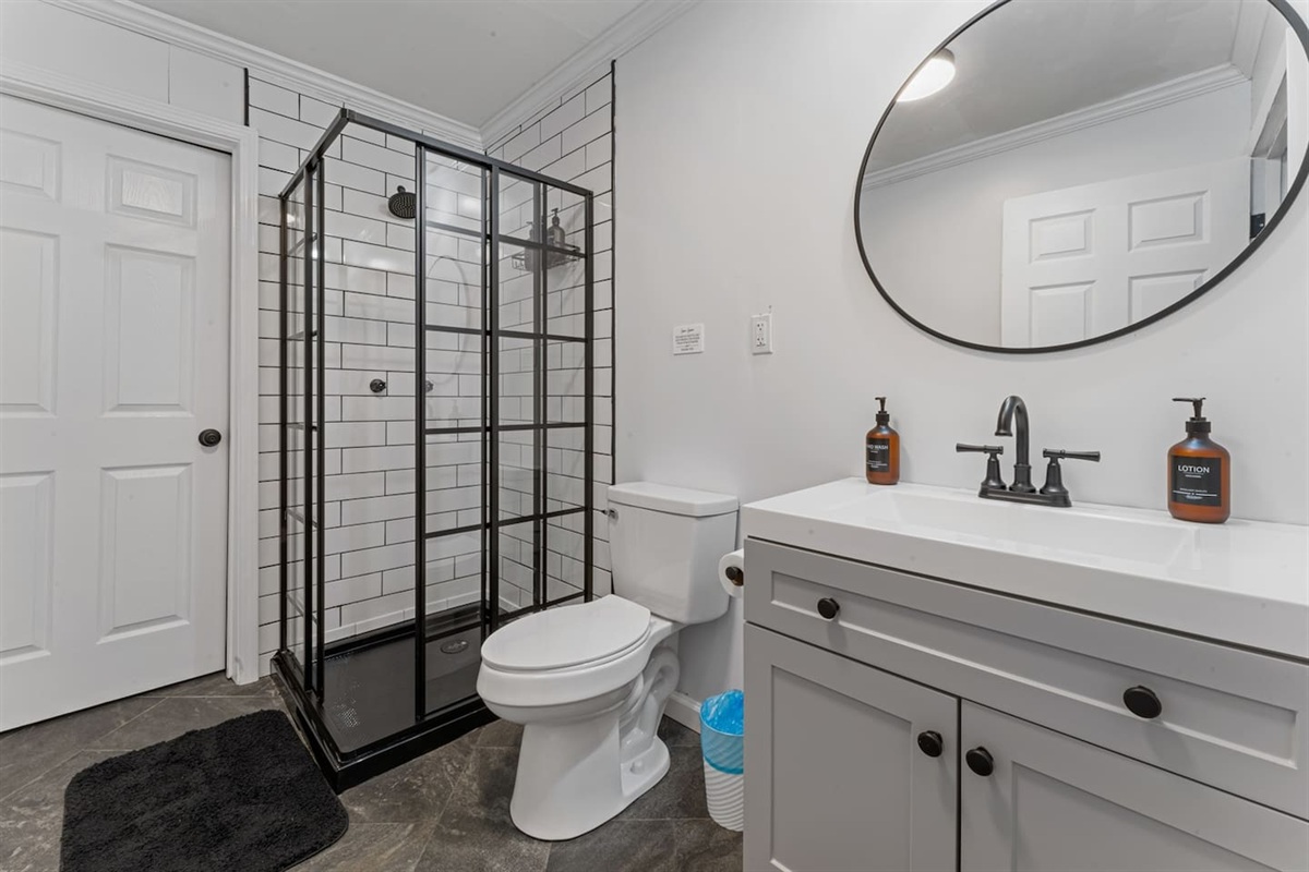 Modern, spotless bathroom featuring a stylish black-framed walk-in shower, spacious vanity, and all essentials provided for a comfortable stay.