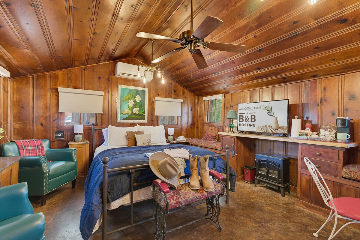Papaw's Cabin knotty pine bedroom with queen bed, cowboy boots, leather armchairs, Keurig coffee bar, and smart TV. Rustic-chic 1930s log cabin stay in Waco, Texas.