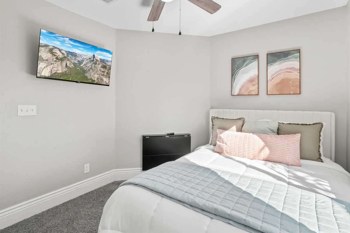 Comfortable bedroom with soft carpeting, a mounted TV for movie nights, and a ceiling fan for added comfort—perfect for relaxing after a busy day.