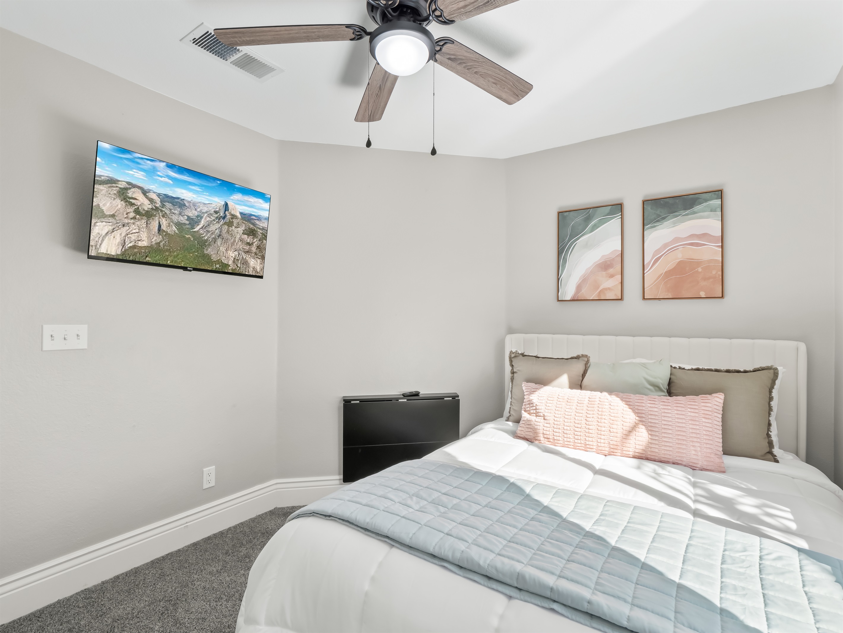 Comfortable bedroom with soft carpeting, a mounted TV for movie nights, and a ceiling fan for added comfort—perfect for relaxing after a busy day.