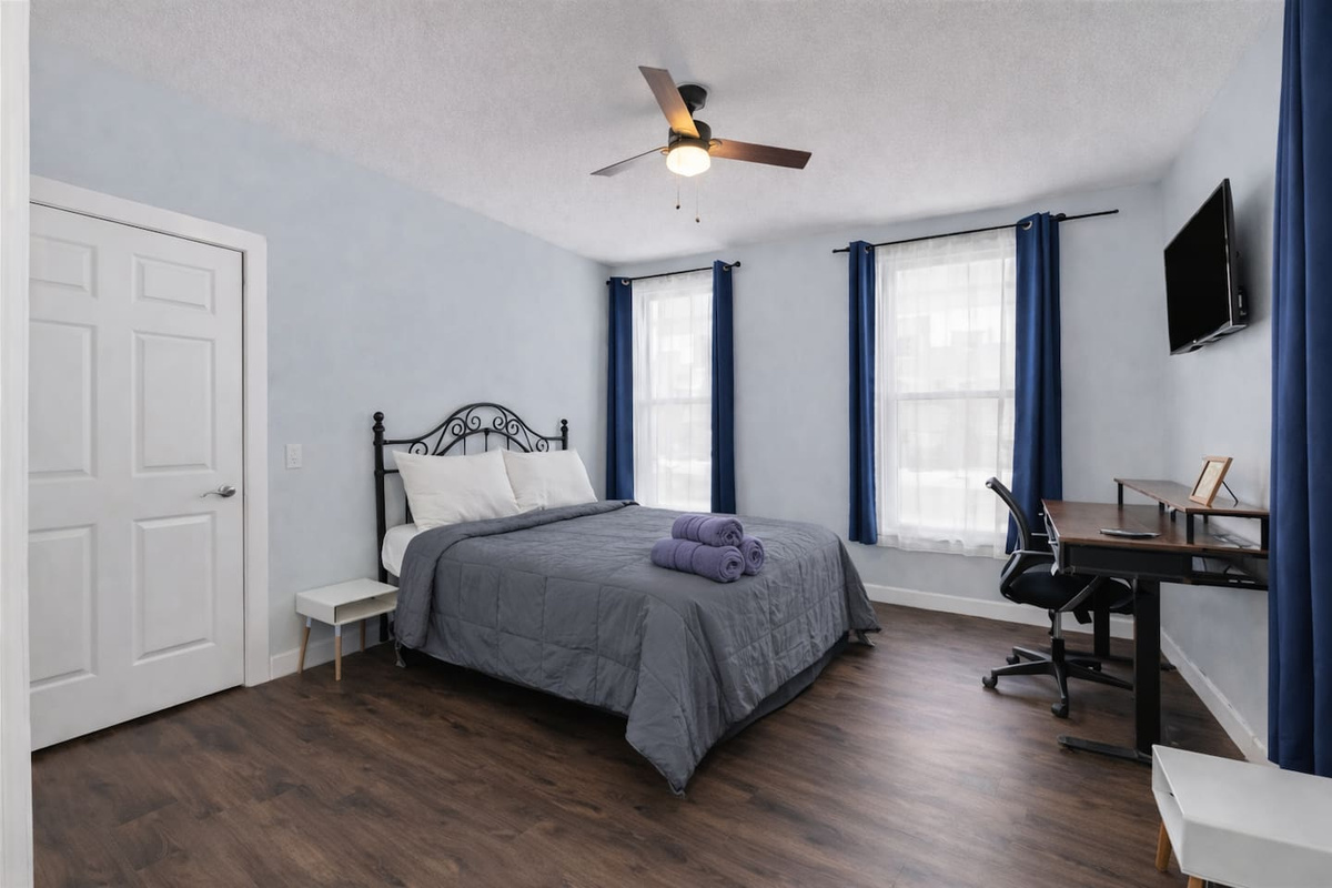 Spacious primary bedroom featuring a comfortable queen-size bed, high ceilings, and warm natural light & work space area.