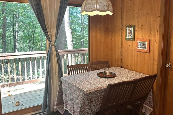 The dining area features a leaf table with four chairs, plus two extras stored in the cabin. It sits in front of a sliding glass door, offering a nice view and natural light. Great for meals, puzzles, or planning your day in the orchard.