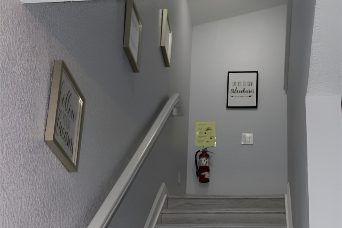 - Stairway with soft gray walls and motivational art for an inviting ascent  
- Wide steps and railing provide safety and ease for all guests  
- Leads to cozy upstairs bedrooms and additional living spaces  
